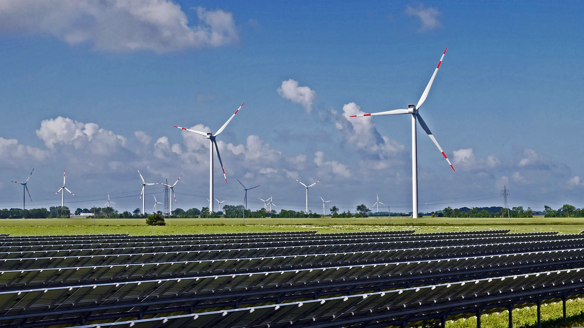 Solar panels in the foreground and wind turbines in the same landscape.